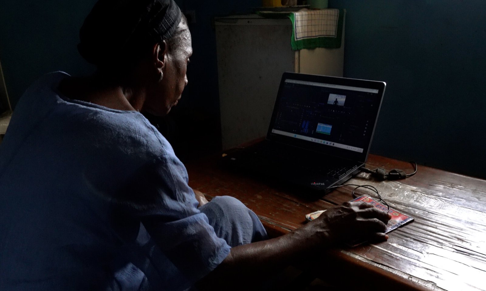 Person seated at a wooden table in a dim room, using a laptop with hands resting near the keyboard